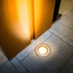 A round light set into a sidewalk illuminating a column built above it.